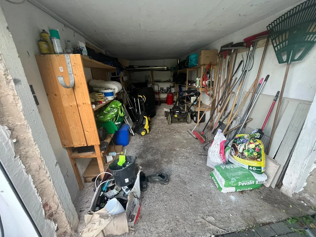 Garage vor der Räumung: Rasenmäher, Hochdruckreiniger, Spaten, Rechen und Säcke mit Pflanzsubstrat